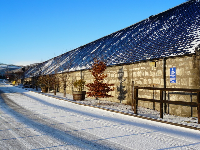 Snow-covered access road beside the long, slate-roofed warehouse buildings at Clynelish Distillery.