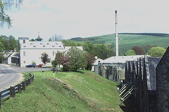 Exterior of Dufftown Distillery in Dufftown, with the main distillery building, plant, chimney and surrounding Speyside hills.
