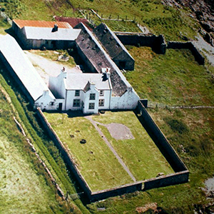 Aerial view of Gartbreck Farm’s white farmhouse and adjoining stone outbuildings on the Loch Indaal shoreline, the planned Gartbreck distillery site on Islay.