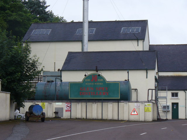 Glen Spey Distillery exterior in Rothes, with cream buildings, dark slate roofs, a tall chimney, and a green Glen Spey sign.