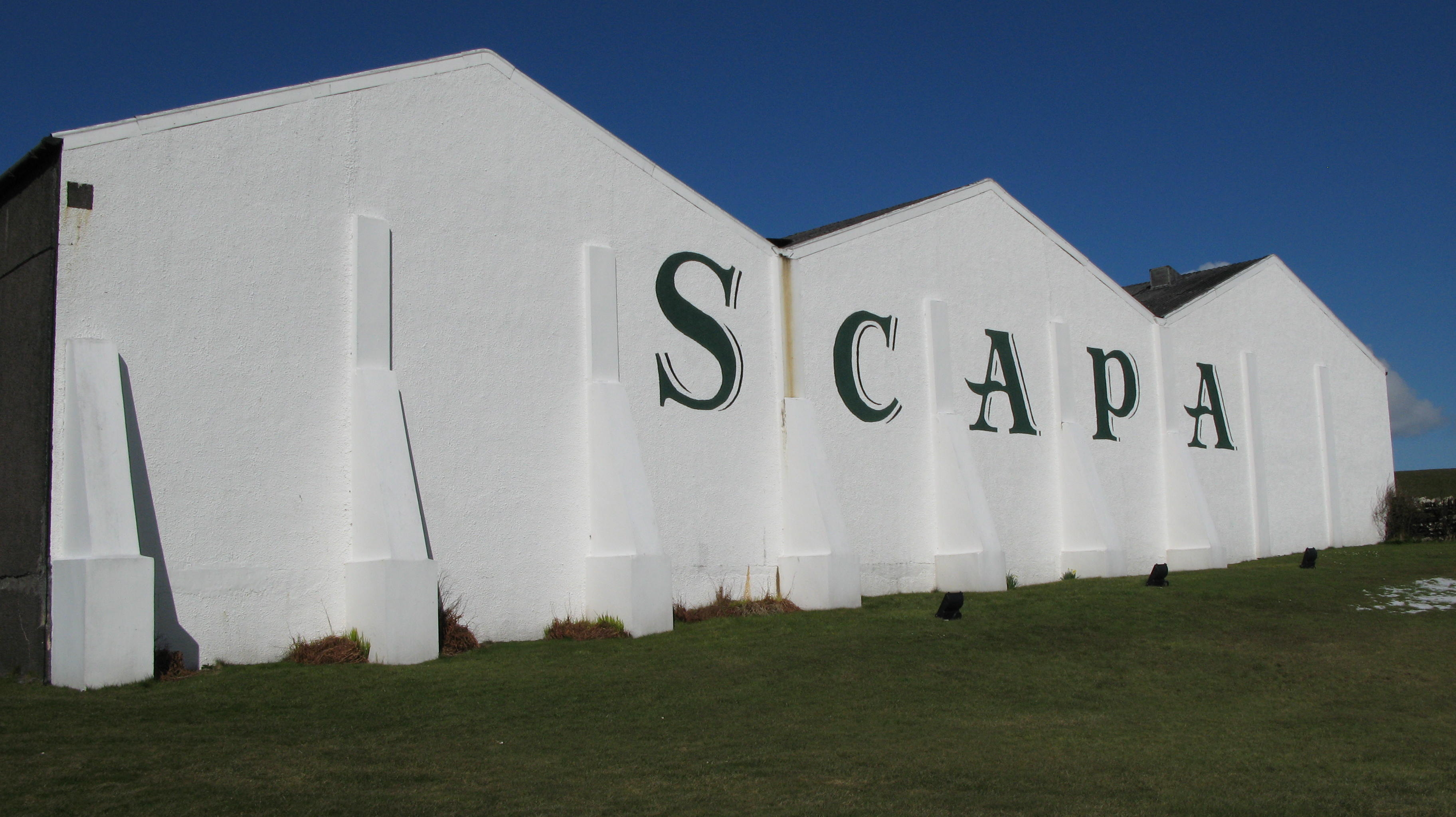 White exterior buildings of Scapa Distillery with large green ‘SCAPA’ lettering.