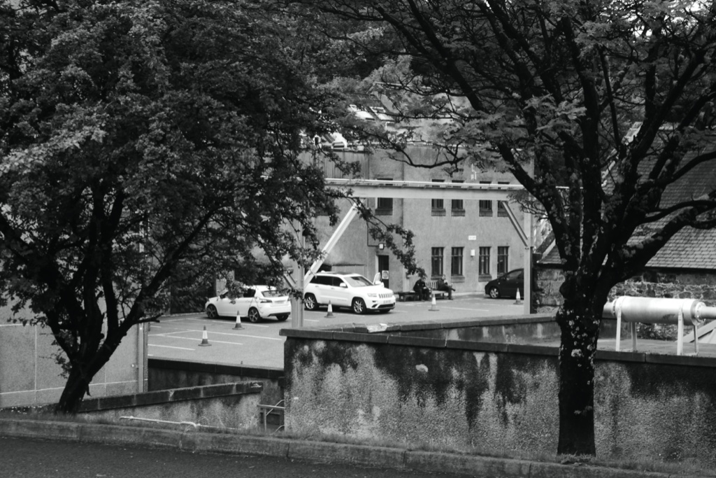 Exterior view of Tamdhu Distillery in Knockando, with the distillery building, paved yard, trees and visible site pipework.