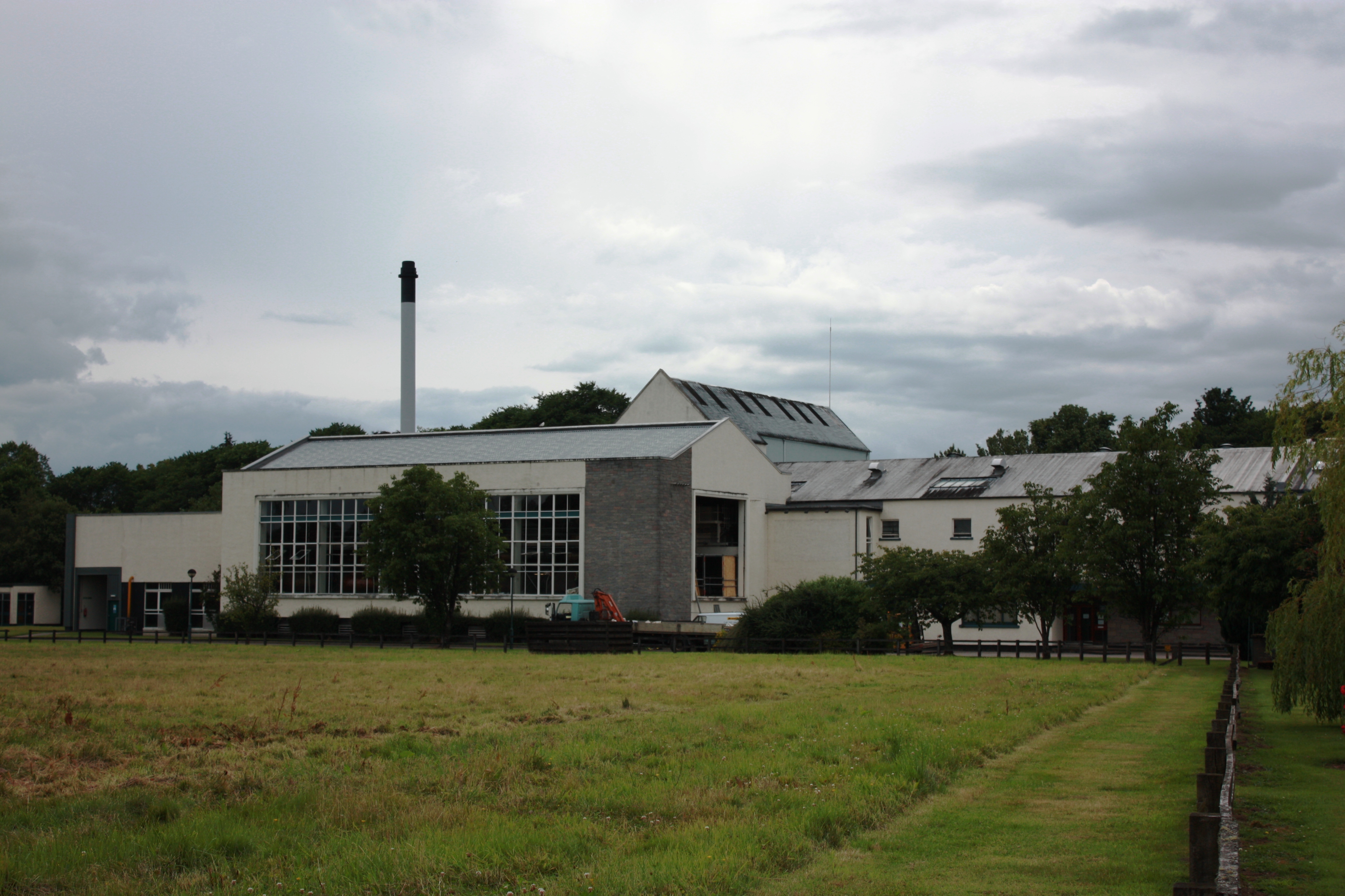 Aerial view of Teaninich Distillery's production buildings near Alness, showing the white distillery complex, chimney, access road, and surrounding Highland landscape.